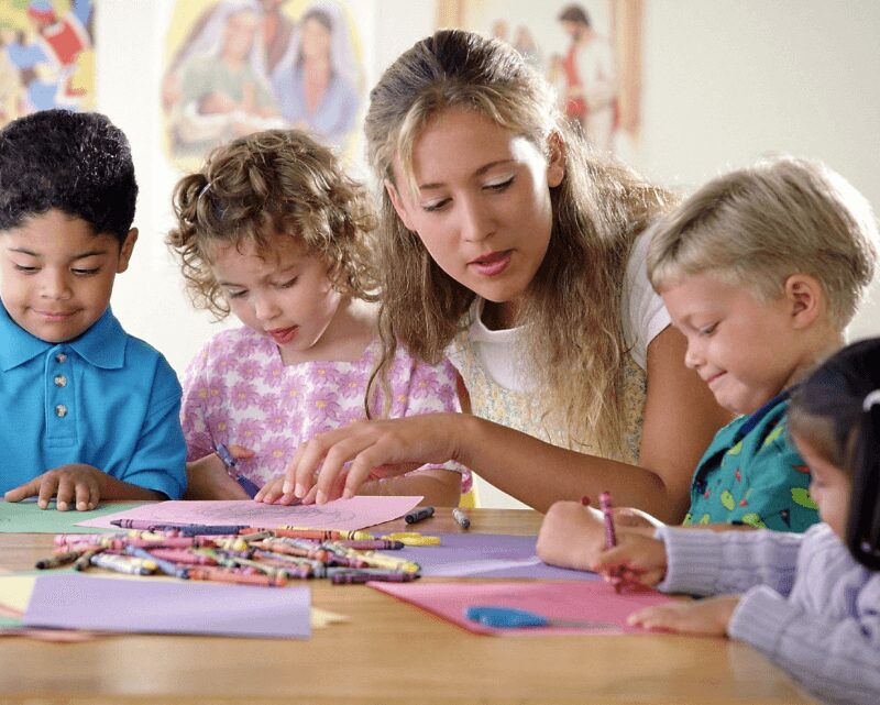 Group of children playing with their teacher in kindergarten